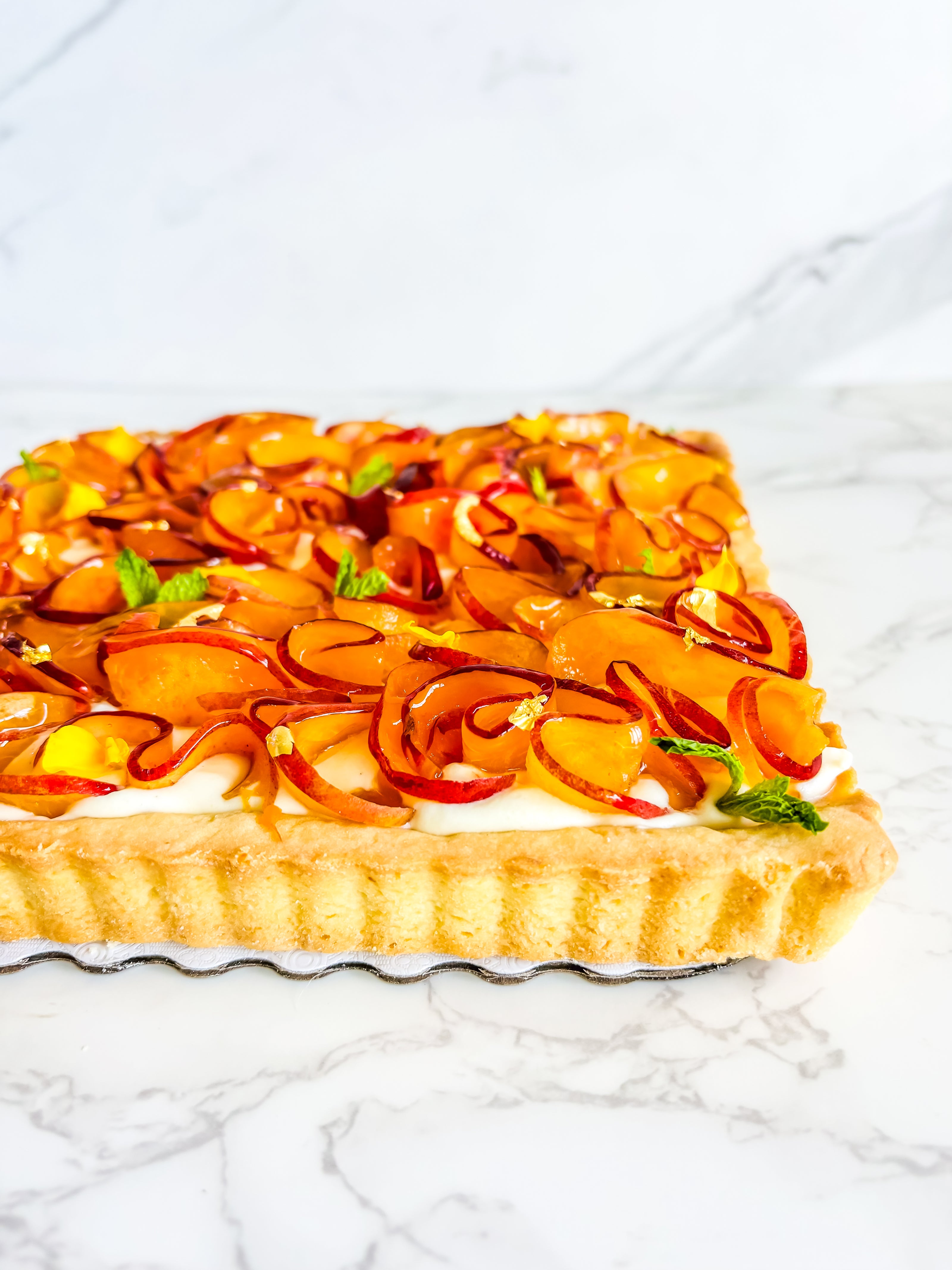 This is a peach shortbread tart. It is made with a lemon buttery shortbread shell and Italian pastry cream filling and decorated with fresh peach ruffles and mini mint leaves. 