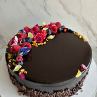 Custom cakes Oahu by Italian pastry chef. This cake is a chocolate sponge cake with chocolate pastry cream filling and a chocolate glaze finish, decorated with fresh berries, edible flowers, and gold leaf. 