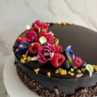 Custom cakes Oahu by Italian pastry chef. This cake is a chocolate sponge cake with chocolate pastry cream filling and a chocolate glaze finish, decorated with fresh berries, edible flowers, and gold leaf.