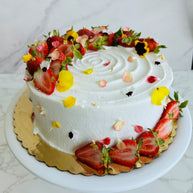 A round strawberry shortcake cake made with vanilla sponge, chantilly filling, and fresh strawberries, decorated with fresh strawberry slices and edible flowers. 
