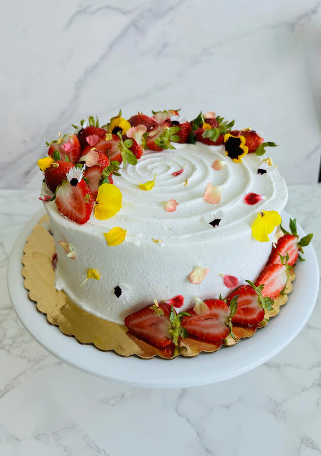 A round strawberry shortcake cake made with vanilla sponge, chantilly filling, and fresh strawberries, decorated with fresh strawberry slices and edible flowers. 