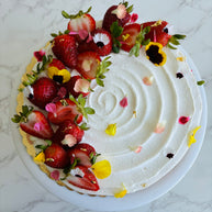 A round strawberry shortcake cake made with vanilla sponge, chantilly filling, and fresh strawberries, decorated with fresh strawberry slices and edible flowers. 