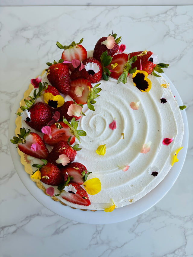 A round strawberry shortcake cake made with vanilla sponge, chantilly filling, and fresh strawberries, decorated with fresh strawberry slices and edible flowers. 