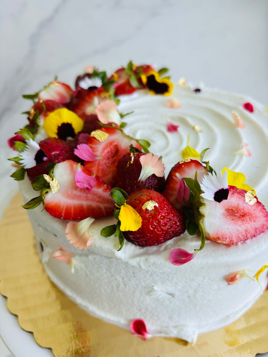 A round strawberry shortcake cake made with vanilla sponge, chantilly filling, and fresh strawberries, decorated with fresh strawberry slices and edible flowers. 