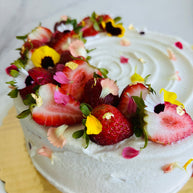 A round strawberry shortcake cake made with vanilla sponge, chantilly filling, and fresh strawberries, decorated with fresh strawberry slices and edible flowers. 