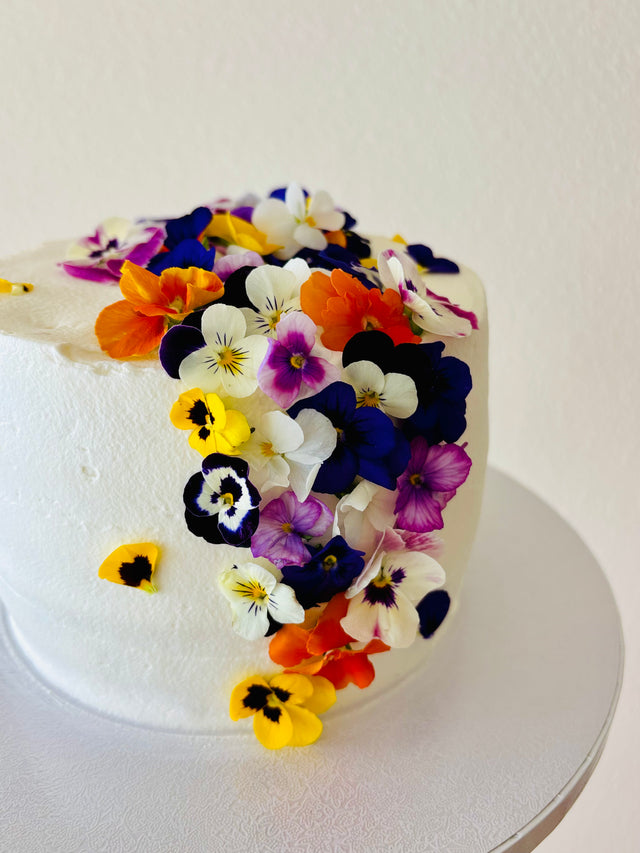 Custom cakes Oahu by an Italian Pastry Chef. This cake is made with vanilla sponge, italian pastry cream filling, elderflower chantilly frosting and decorated with edible pansies  and violas flowers.