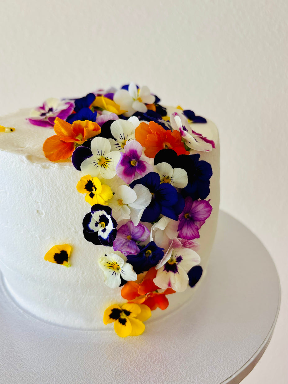 Custom cakes Oahu by an italian Pastry Chef. This cake is made with vanilla sponge, italian pastry cream filling, elderflower chantilly frosting and decorated with edible pansies  and violas flowers.