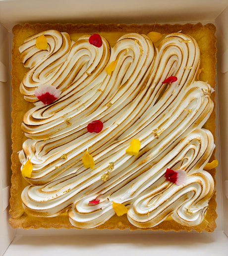This is a lemon meringue shortbread tart. It is made with lemon-vanilla shortbread, has a lemon curd filling, and has a torched Italian meringue top layer. It is decorated with edible flowers and gold leaf flakes. 