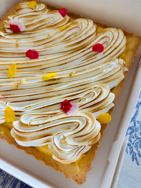 This is a lemon meringue shortbread tart. It is made with lemon-vanilla shortbread, has a lemon curd filling, and has a torched Italian meringue top layer. It is decorated with edible flowers and gold leaf flakes. 