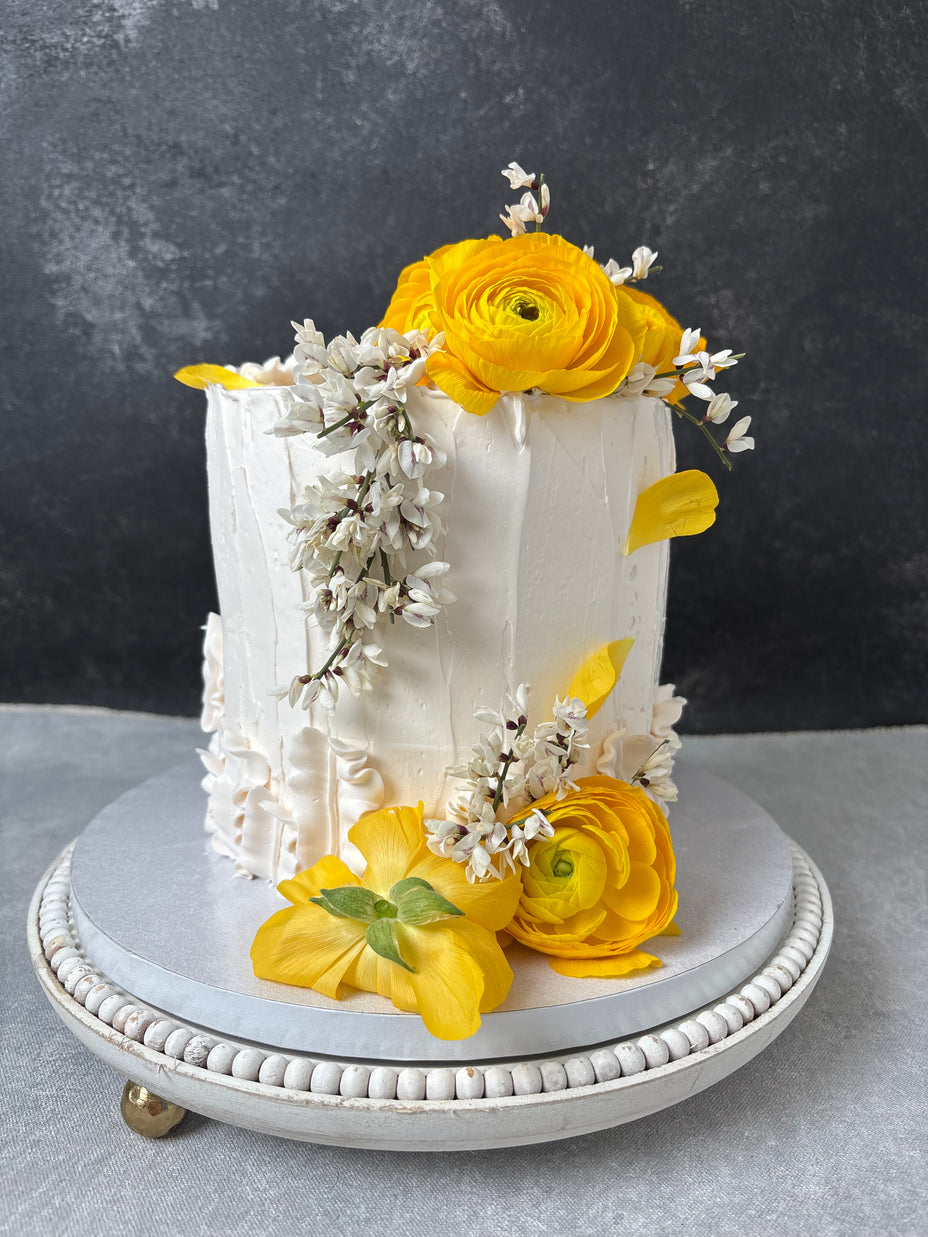 One tiered round custom cake. Made of vanilla sponge, white chocolate chantilly filling and fresh raspberries. Decorated with vanilla buttercream and fresh flowers.