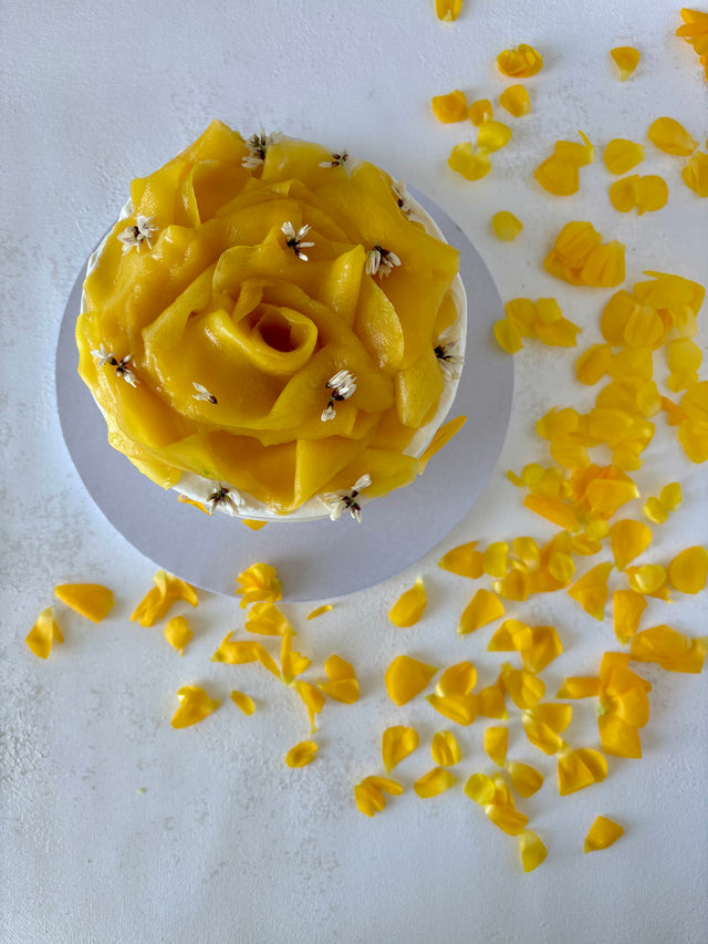 This is a round vanilla and mango cake. It is made of vanilla sponge, white chocolate chantilly, and fresh mango bites. It is decorated with a flower made of mango slices and fresh edible flowers.