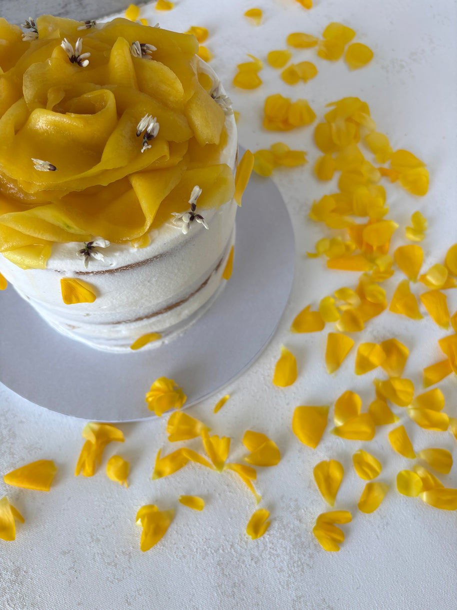 This is a round vanilla and mango cake. It is made of vanilla sponge, white chocolate chantilly, and fresh mango bites. It is decorated with a flower made of mango slices and fresh edible flowers.