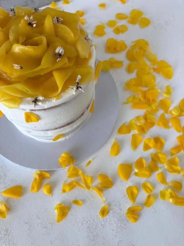 This is a round vanilla and mango cake. It is made of vanilla sponge, white chocolate chantilly, and fresh mango bites. It is decorated with a flower made of mango slices and fresh edible flowers.