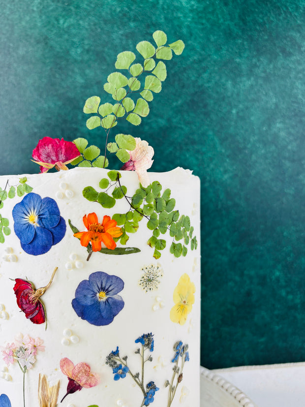 One tier white round cake. The cake is decorated with beautiful pressed flowers.