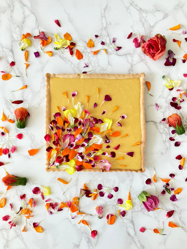 This is a square shortbread tart made with a lemony shortbread shell, a fresh Hawaiian mango filling, decorated with a garden of edible flower petals. 
