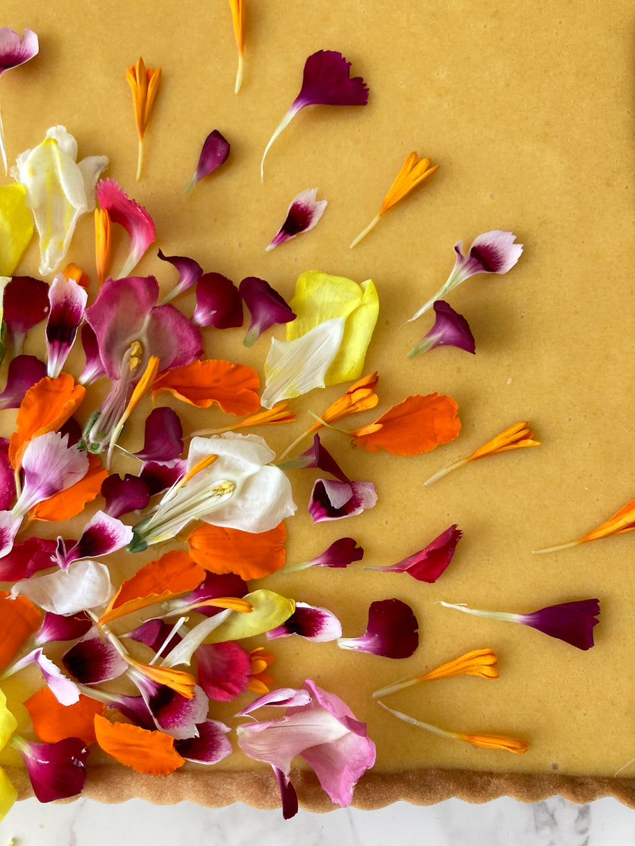This is a square shortbread tart made with a lemony shortbread shell, a fresh Hawaiian mango filling, decorated with a garden of edible flower petals. 