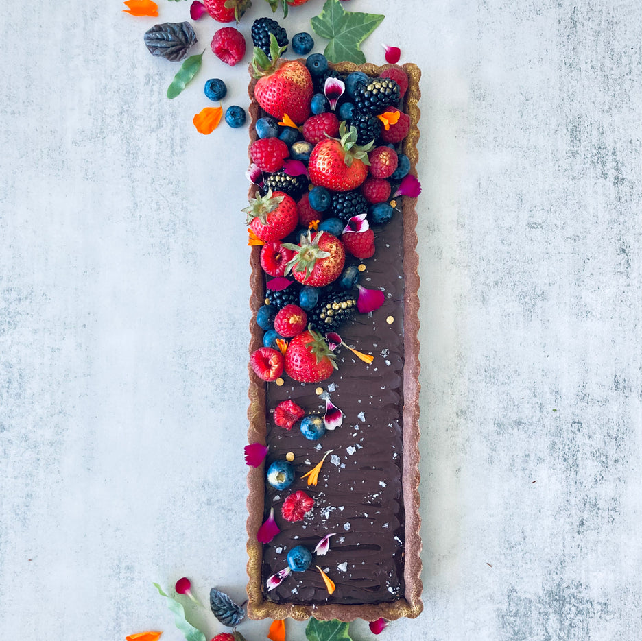 A rectangular chocolate tart with a buttery chocolate shell and rich chocolate ganache filling, decorated with fresh mixed berries, edible flowers, and Maldon salt flakes. 