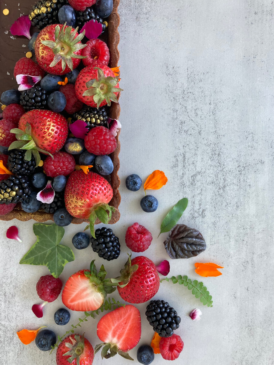 A rectangular chocolate tart with a buttery chocolate shell and rich chocolate ganache filling, decorated with fresh mixed berries, edible flowers, and Maldon salt flakes. 