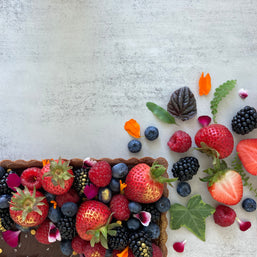 A rectangular chocolate tart with a buttery chocolate shell and rich chocolate ganache filling, decorated with fresh mixed berries, edible flowers, and Maldon salt flakes. 