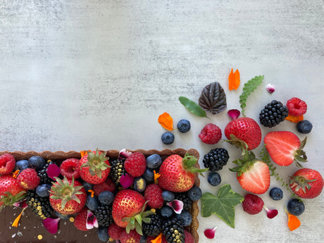 A rectangular chocolate tart with a buttery chocolate shell and rich chocolate ganache filling, decorated with fresh mixed berries, edible flowers, and Maldon salt flakes. 